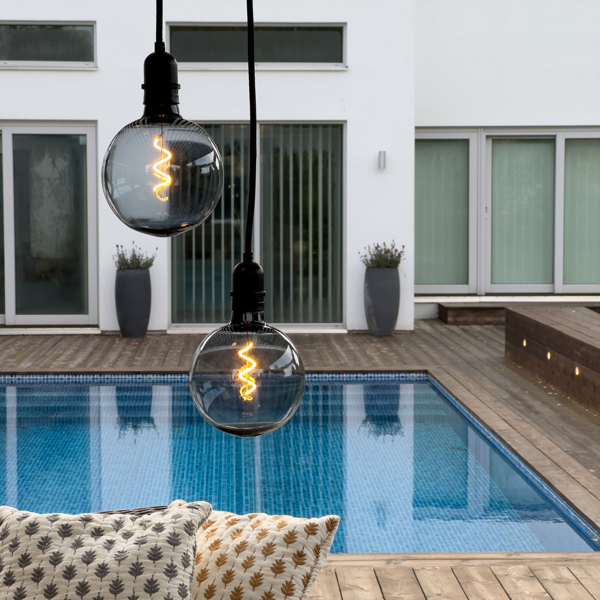 Hängande rökfärgade globlampor som lyser stämningsfullt över en pool