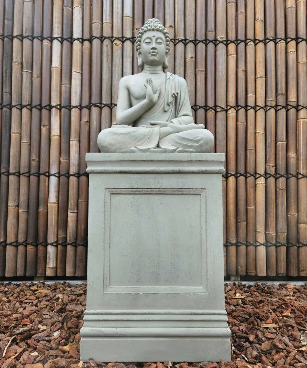 Stor grå trädgårdsfigur föreställande Buddha på en matchande piedestal
