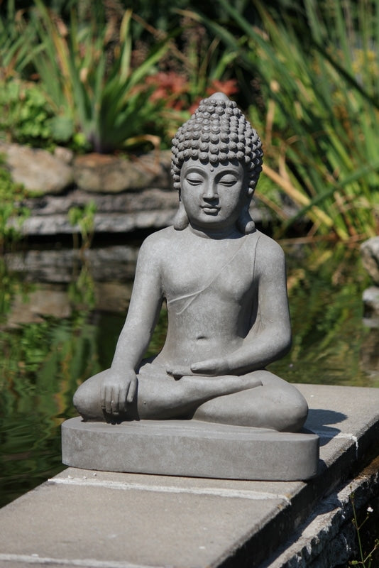 Meditativ Buddha figurin placerad vid en trädgårdsdamm för harmonisk utemiljö