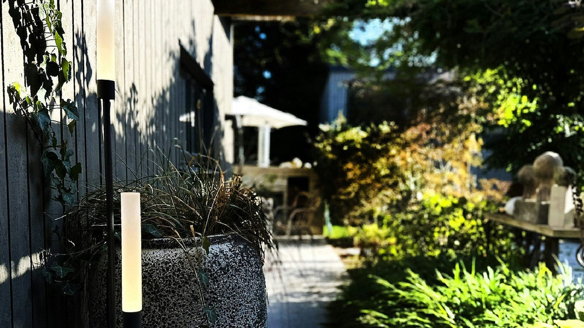 Eleganta ljuspelare placerade i en stor kruka vid sommarstugans grå träfasad