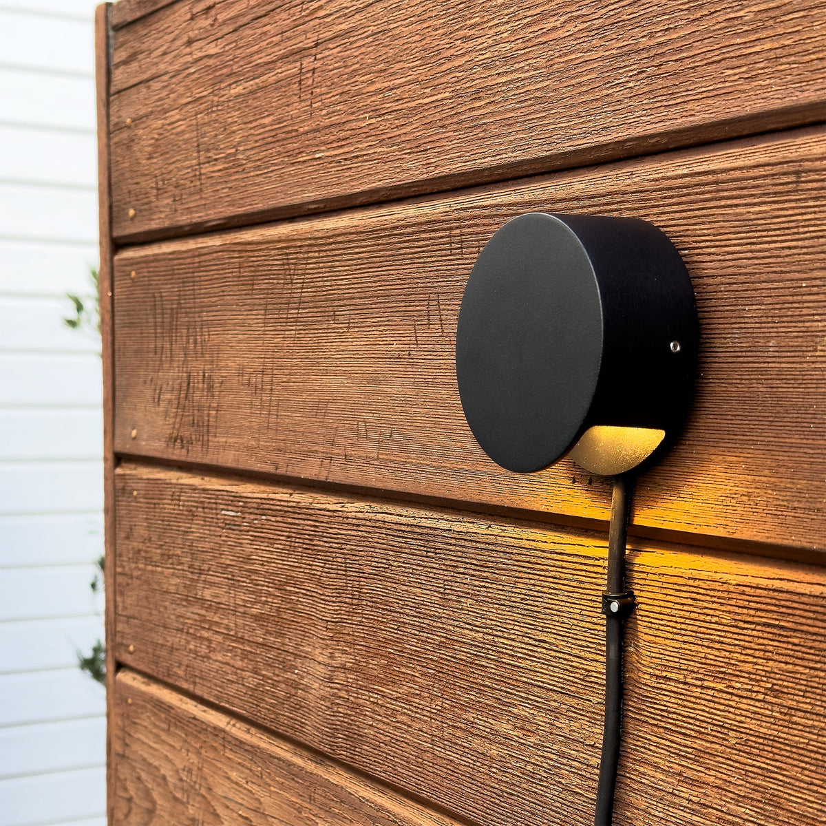 Nero trädgårdslampa installerad på ett staket som lyser upp växter