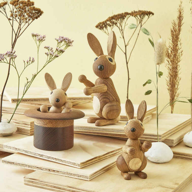 Tre kaninfigurer i trä och en hög hatt placerade bland torkade blommor