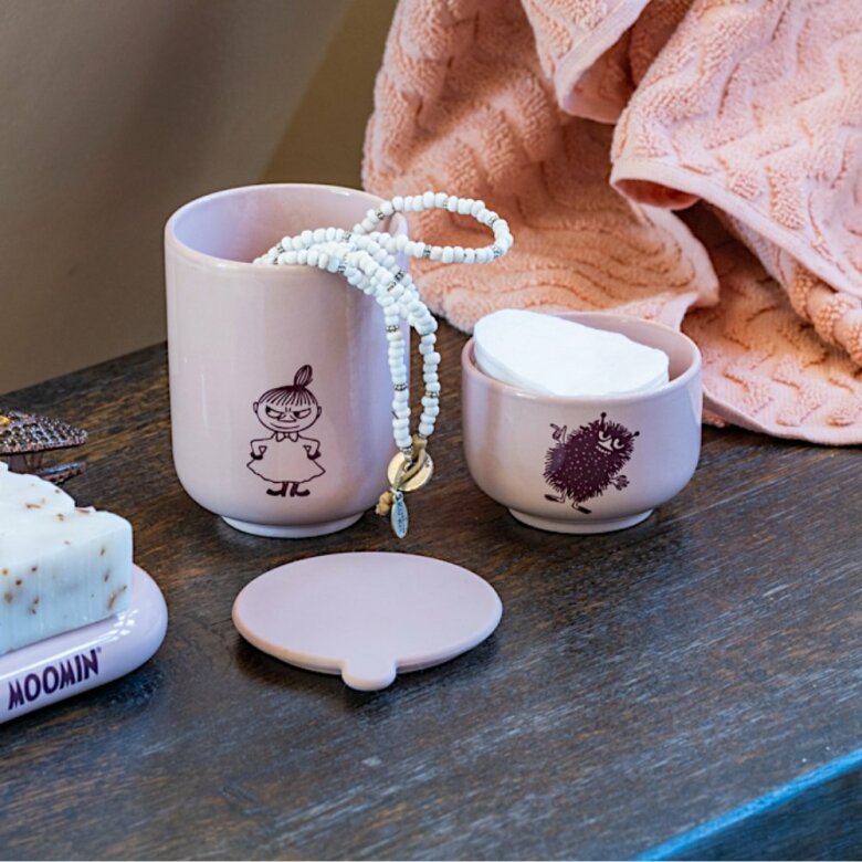 Liten rosa skål med Stinky bredvid en Mumin-mugg och ett pärlhalsband