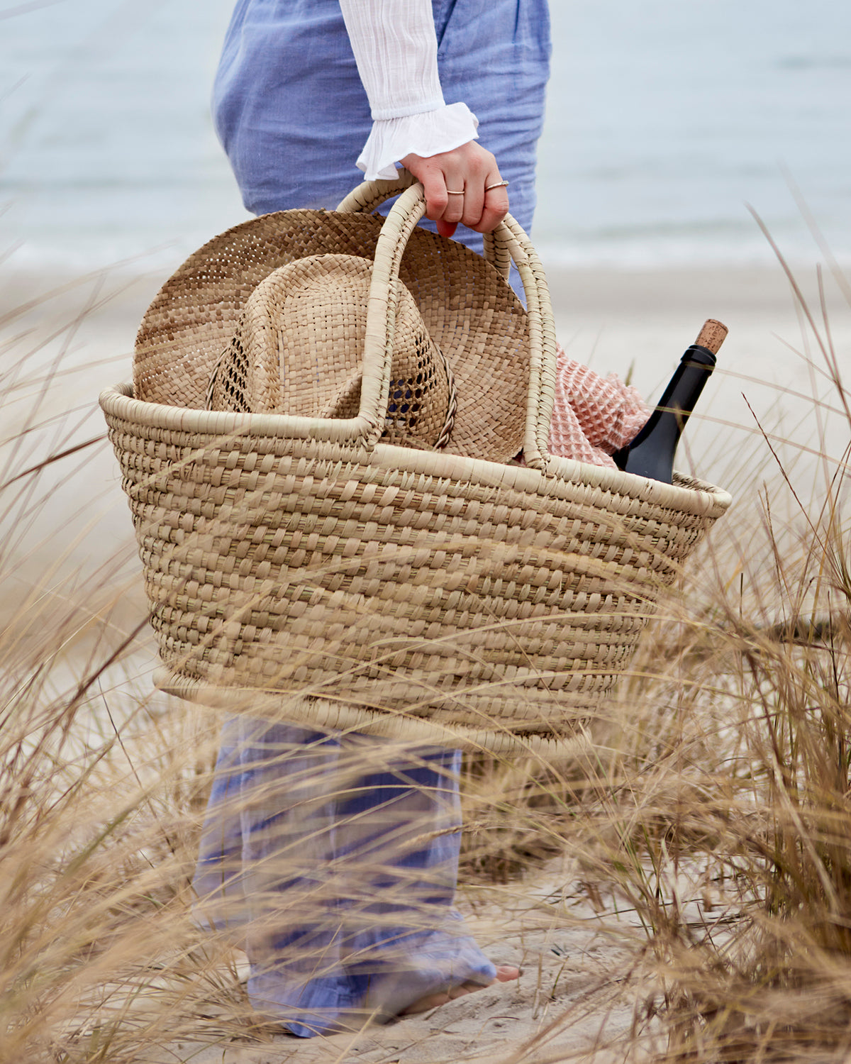 Flätad picknickkorg med stråhatt och filt på en sandstrand