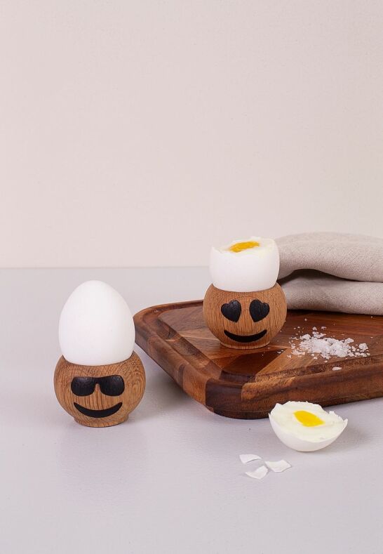 Två äggkoppar i ek med emojis på en rustik träskärbräda i ett lantkök
