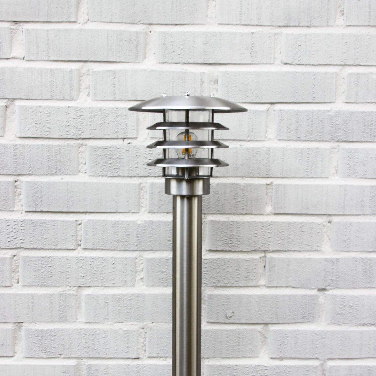 LightsOn Saturnus pollare i silver installerad invid en blomsterrabatt