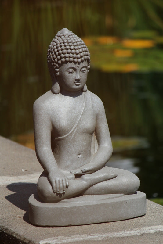 Närbild på en grå Buddhastaty i stenlook som pryder en stenkant utomhus