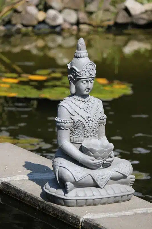 Ljusgrå Guanyin skulptur placerad vid en trädgårdsdamm i solljus
